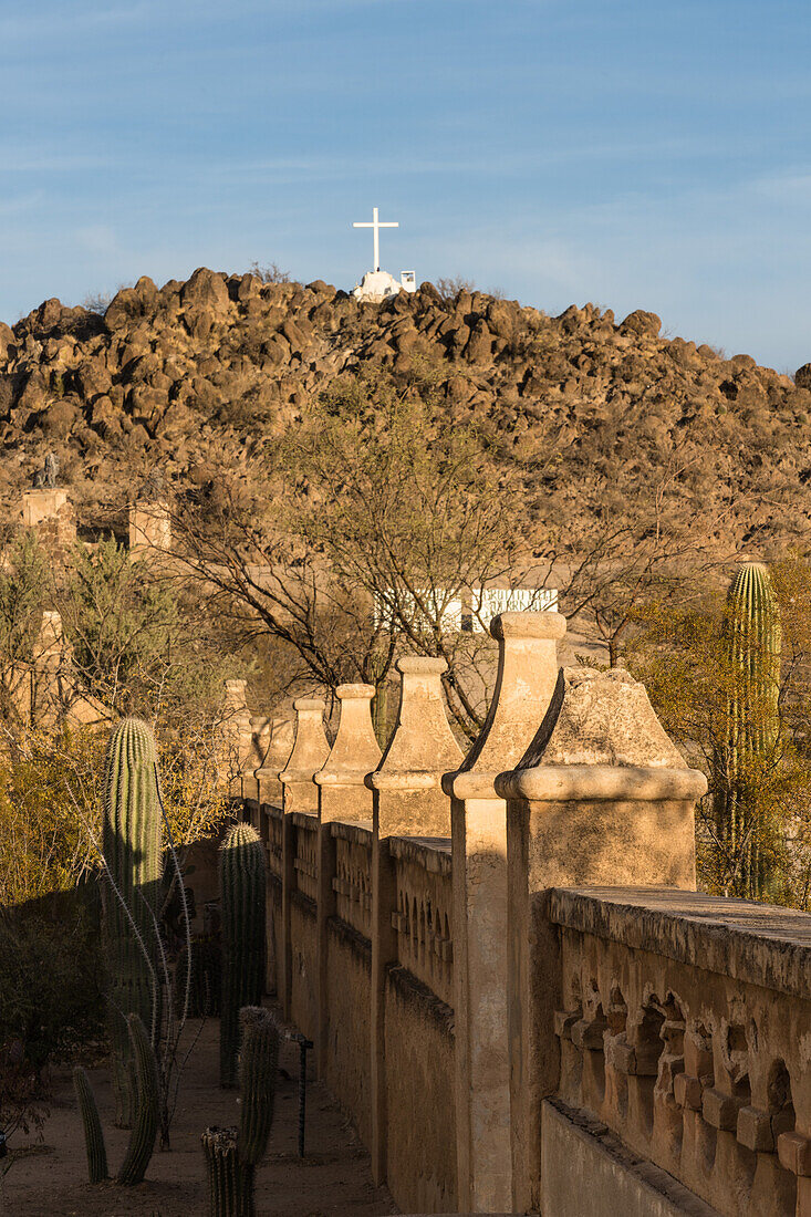 The Grotto Hill with its white cross outside the protective wall of the Mission San Xavier del Bac, Tucson Arizona.