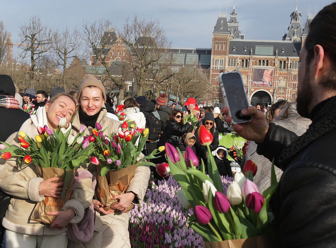Zwei Frauen posieren für ein Foto, während Tausende von Menschen während des nationalen Tulpentages auf dem Museumsplatz in der Nähe des Rijskmuseums am 20. Januar 2024 in Amsterdam, Niederlande, kostenlos Tulpen pflücken. Heute ist der offizielle Beginn der Tulpensaison mit einem speziellen Tulpengarten, in dem die Menschen kostenlos Tulpen pflücken können. In diesem Jahr wird der 12. Jahrestag des von den niederländischen Tulpenzüchtern organisierten Pflückgartens besonders gefeiert. Der Amsterdamer Museumsplatz ist mit rund 200.000 Tulpen gefüllt. Diese Tulpen werden speziell zu einem riesi