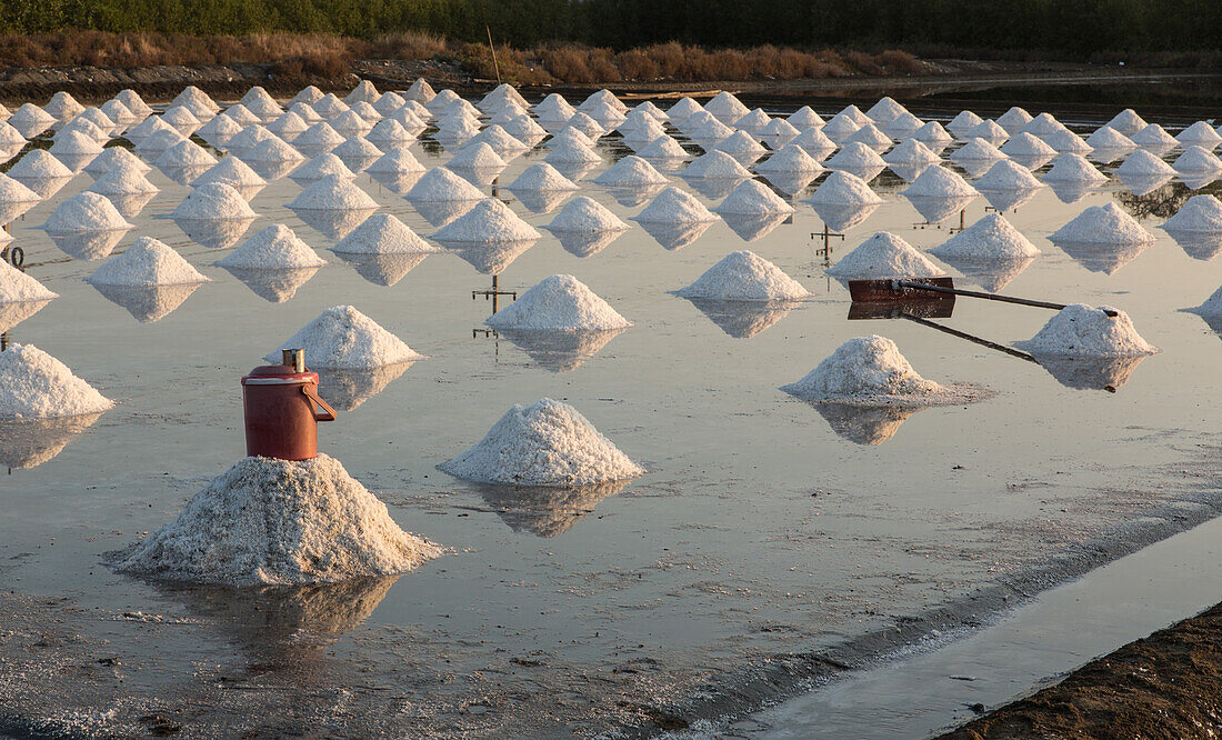 Piles of salt, a water cooler and a scraper at a traditional salt farm in Samut Sakhon, Thailand.