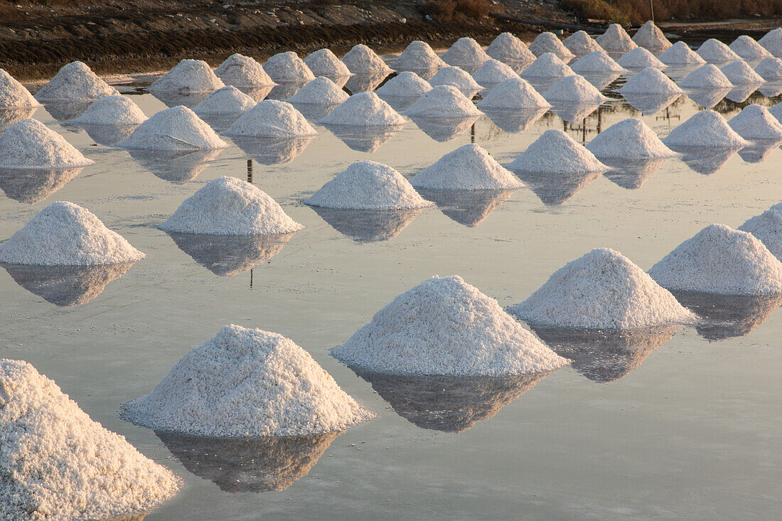 Piles of salt create geometric designs on the salt pan at a traditional evaporation salt farm in Samut Sakhon, Thailand.