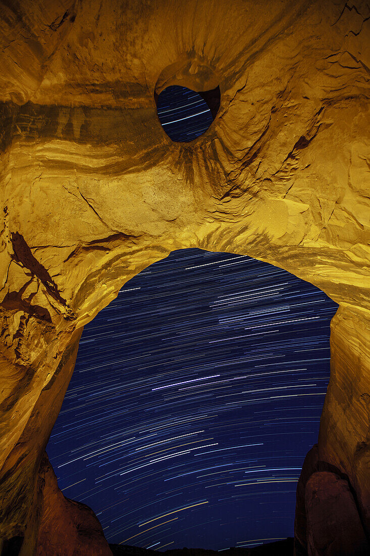 Star trails through the Big Hogan Arch at night in the Monument Valley Navajo Tribal Park in Arizona.