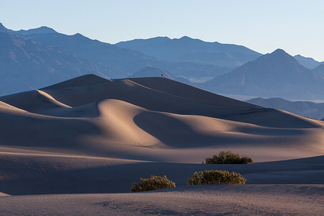 Sunrise on the Mesquite Flat sand dunes in Death Valley National Park in the Mojave Desert, California. Two hikers are on the dunes.