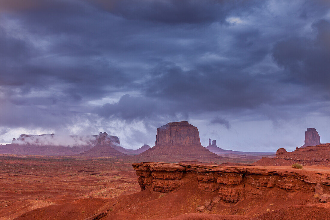 Stürmischer Blick auf das Monument Valley vom John Ford Point im Monument Valley Navajo Tribal Park in Arizona. V.l.n.r.: Sentinal Mesa mit dem West Mitten im Vordergrund, Big Indian Chief durch Wolken verdeckt, Merrick Butte, das Schloss, die Postkutsche und der East Mitten. John Ford Point befindet sich im Vordergrund.
