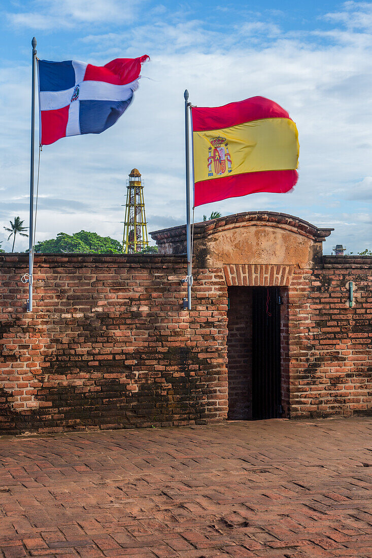 Flags of the Dominican Republic and Spain at Fortaleza San Felipe, now a museum at Puerto Plata, Dominican Republic. In the background is the cast iron lighthouse from 1879.