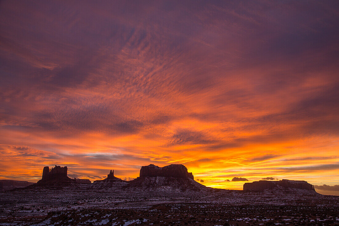 Colorful sunset skies over the Utah monuments in the Monument Valley Navajo Tribal Park in Utah & Arizona. L-R: Castle Butte & the Stagecoach, King on the Throne, Brigham's Tomb & Eagle Mesa.