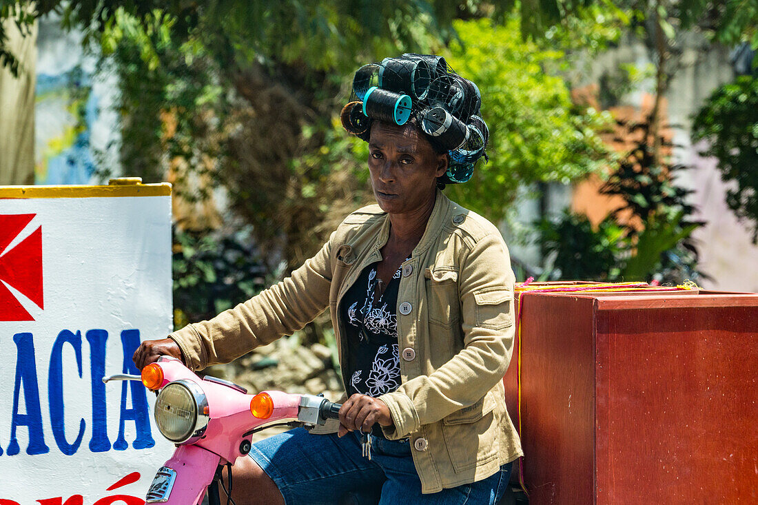 A Dominican woman with her hair up in curlers on a motorcycle in the Dominican Republic.