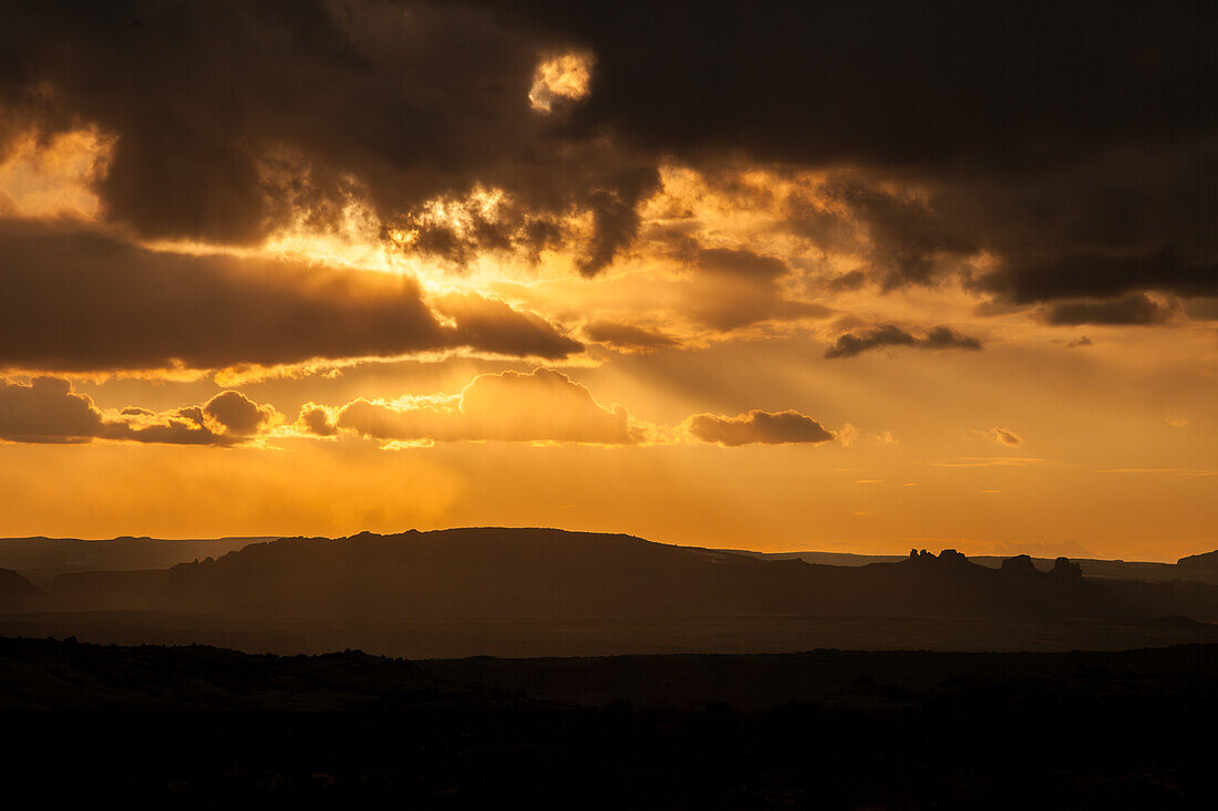 Sonnenstrahlen, die bei Sonnenuntergang über der Canyonlandschaft um Moab, Utah, durch die Wolken dringen