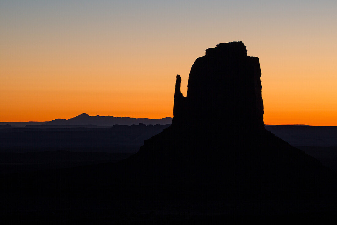 Pastel sunrise sky behind the East Mitten Butte in the Monument Valley Navajo Tribal Park in Arizona.