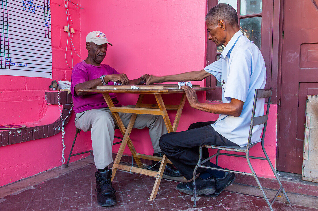 Zwei ältere dominikanische Männer spielen eine Partie Domino auf der Veranda eines Gebäudes in Puerto Plata, Dominikanische Republik. Domino ist der nationale Zeitvertreib in der Dominikanischen Republik.