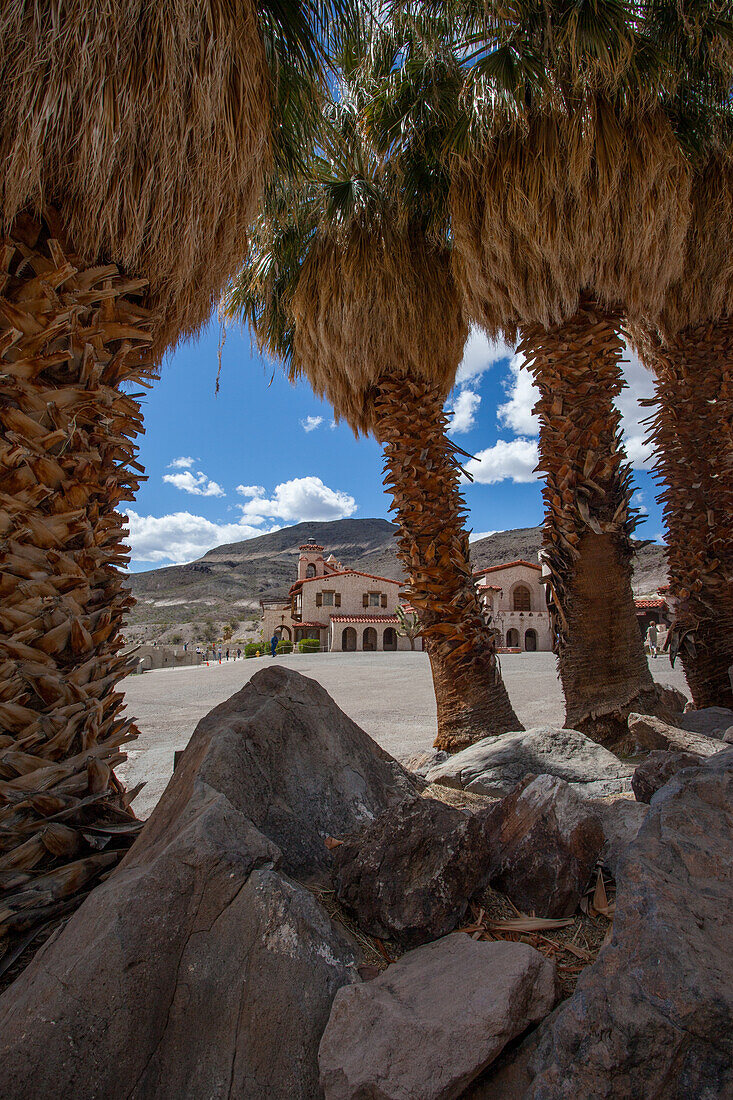 Kalifornische Fächerpalmen umrahmen Scotty's Castle, ein historisches Herrenhaus im Death Valley National Park in der Mojave-Wüste, Kalifornien