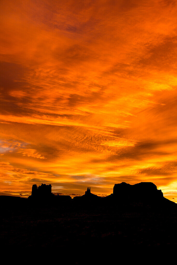 Colorful sunset skies over the Utah monuments in the Monument Valley Navajo Tribal Park in Utah & Arizona. L-R: Castle Butte & the Stagecoach, King on the Throne & Brigham's Tomb.