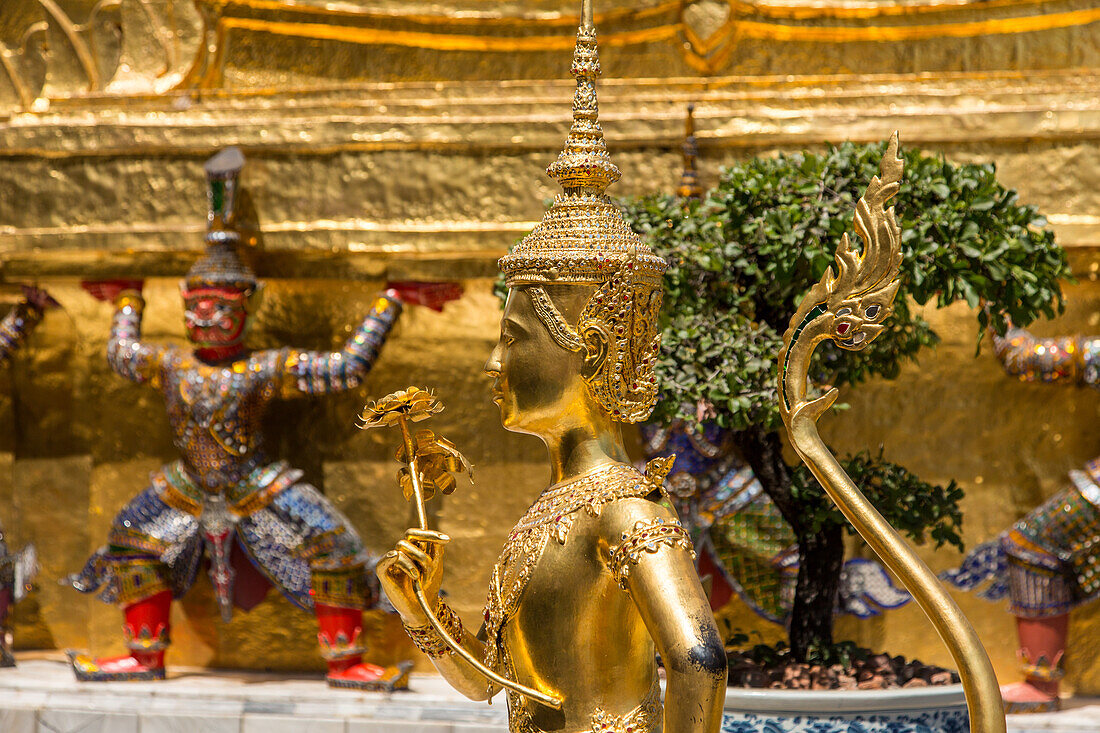 Golden statue of a mythical Thepnorasi guards the Temple of the Emerald Buddha in the Grand Palace complex in Bangkok, Thailand.