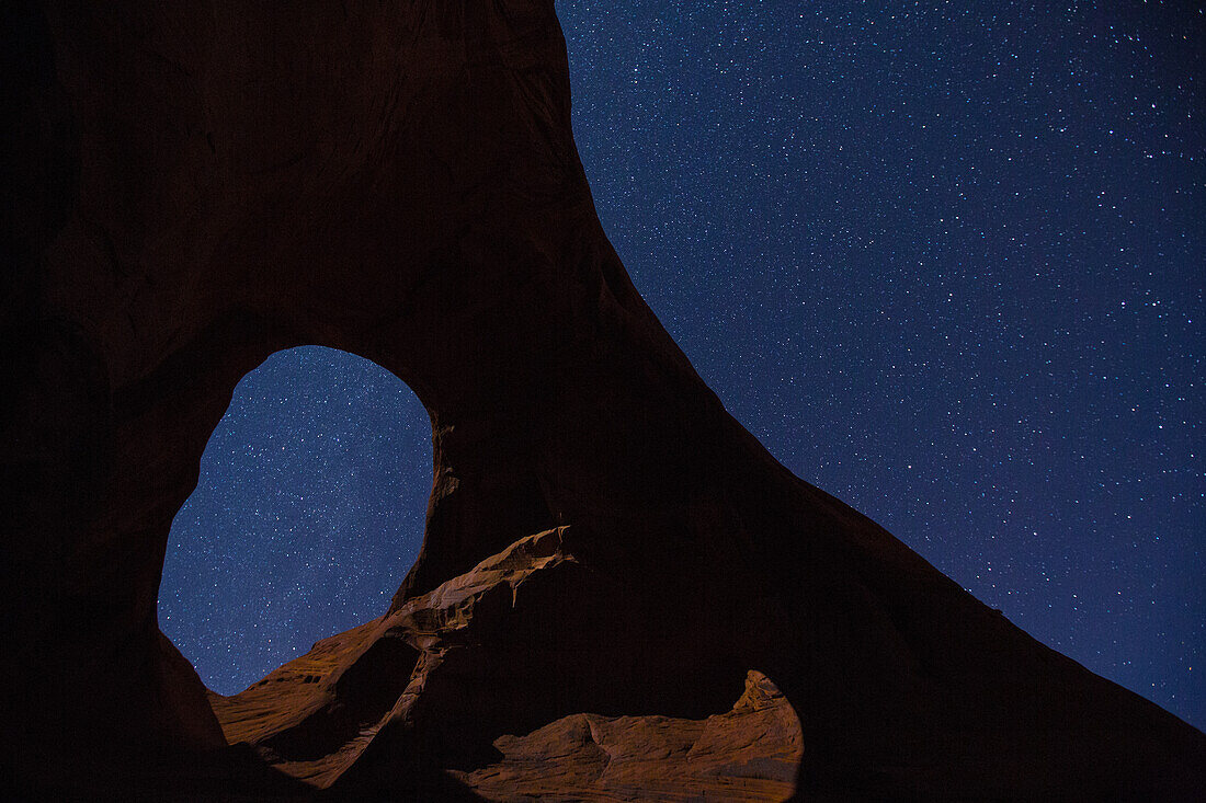 Sterne und Mond leuchten durch den Ear of the Wind Arch bei Nacht im Monument Valley Navajo Tribal Park in Arizona