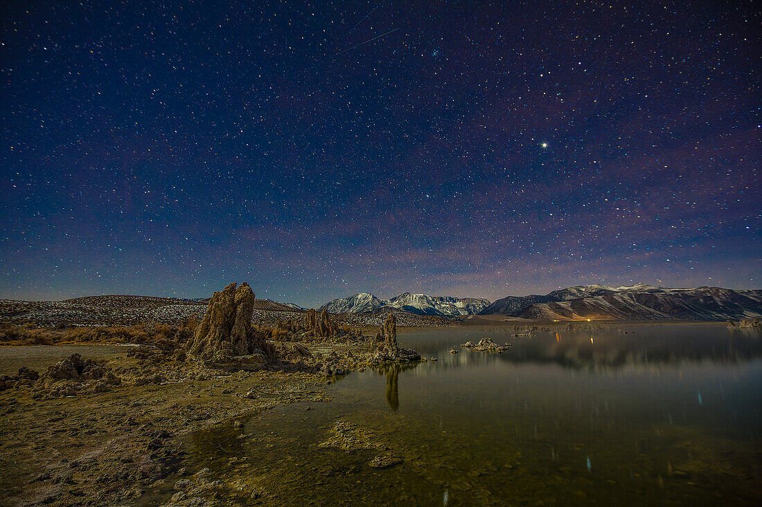 Stars over moonlit tufa formations in Mono Lake in California with the Eastern Sierra Mountains behind.