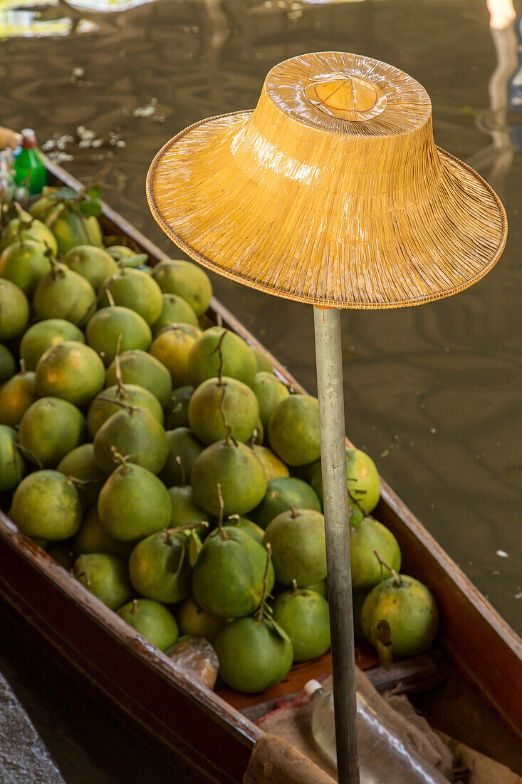 Ein traditioneller thailändischer Hut und Sapodilla-Früchte, die auf einem Boot auf dem schwimmenden Markt von Damnoen Saduak in Thailand verkauft werden