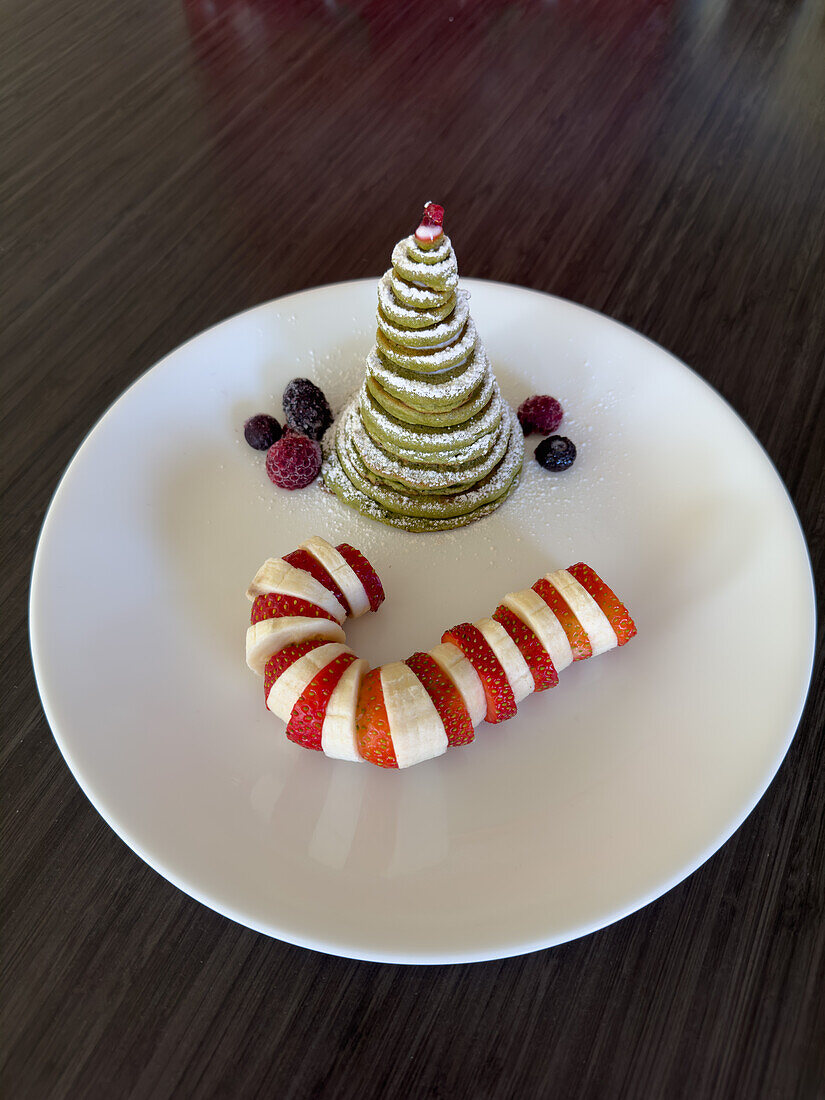 A Christmas holiday breakfast with a pancake Christmas tree and a banana & strawberry candy cane.