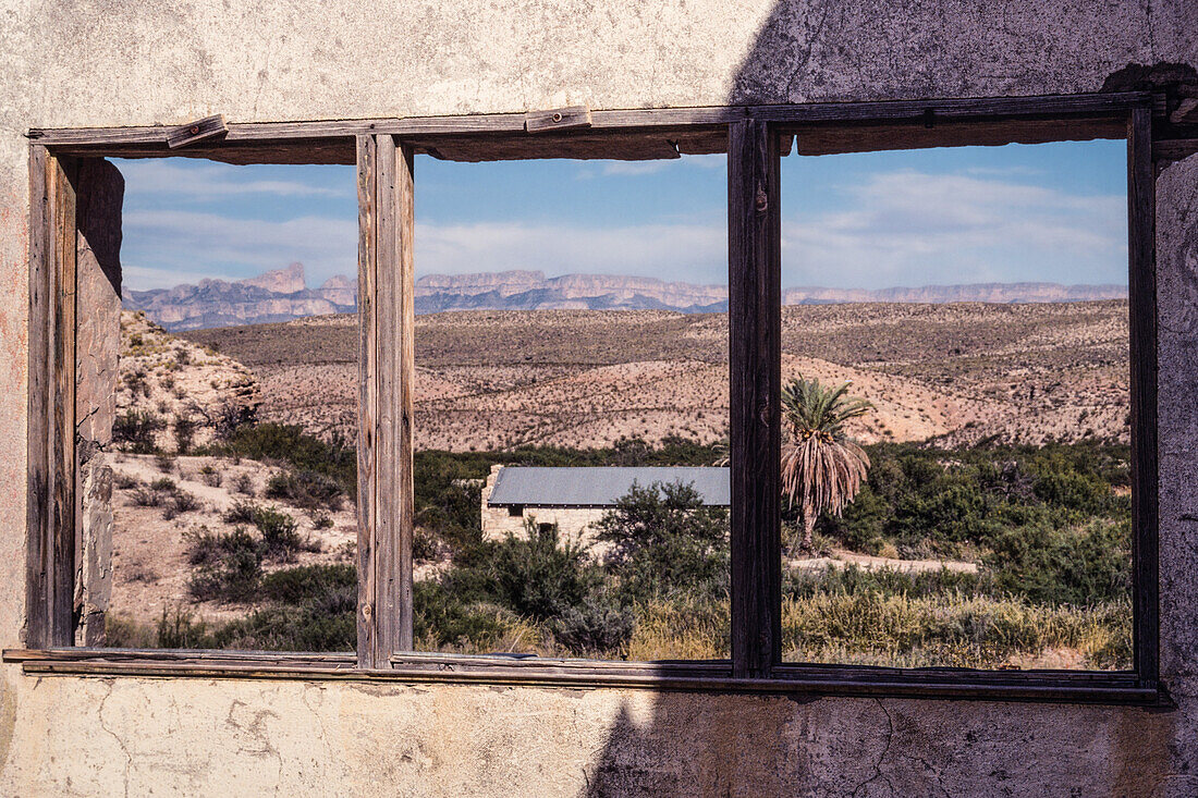 Das Fenster einer alten Ruine in Hot Springs umrahmt die Wüstenlandschaft und das alte Postamt im Big Bend National Park in Texas. In der Ferne sind die Berge der Sierra del Carmen in Mexiko zu sehen.