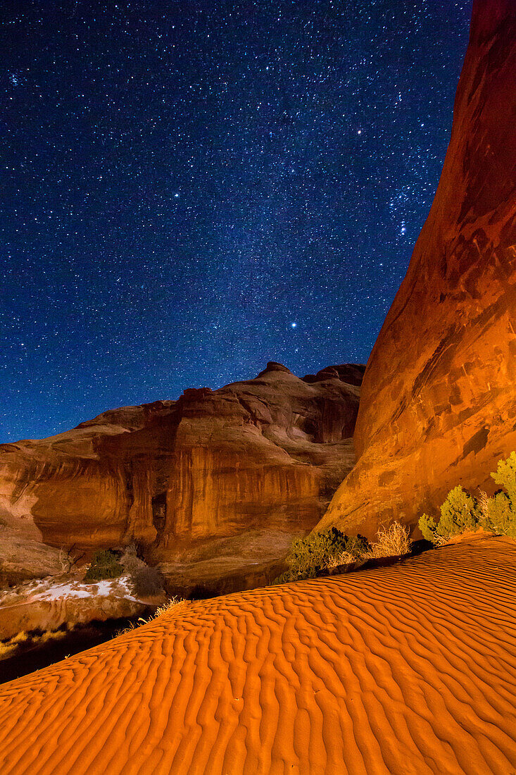 Orion & the Milky Way over the sand by the Ear of the Wind Arch at night in the Monument Valley Navajo Tribal Park in Arizona.