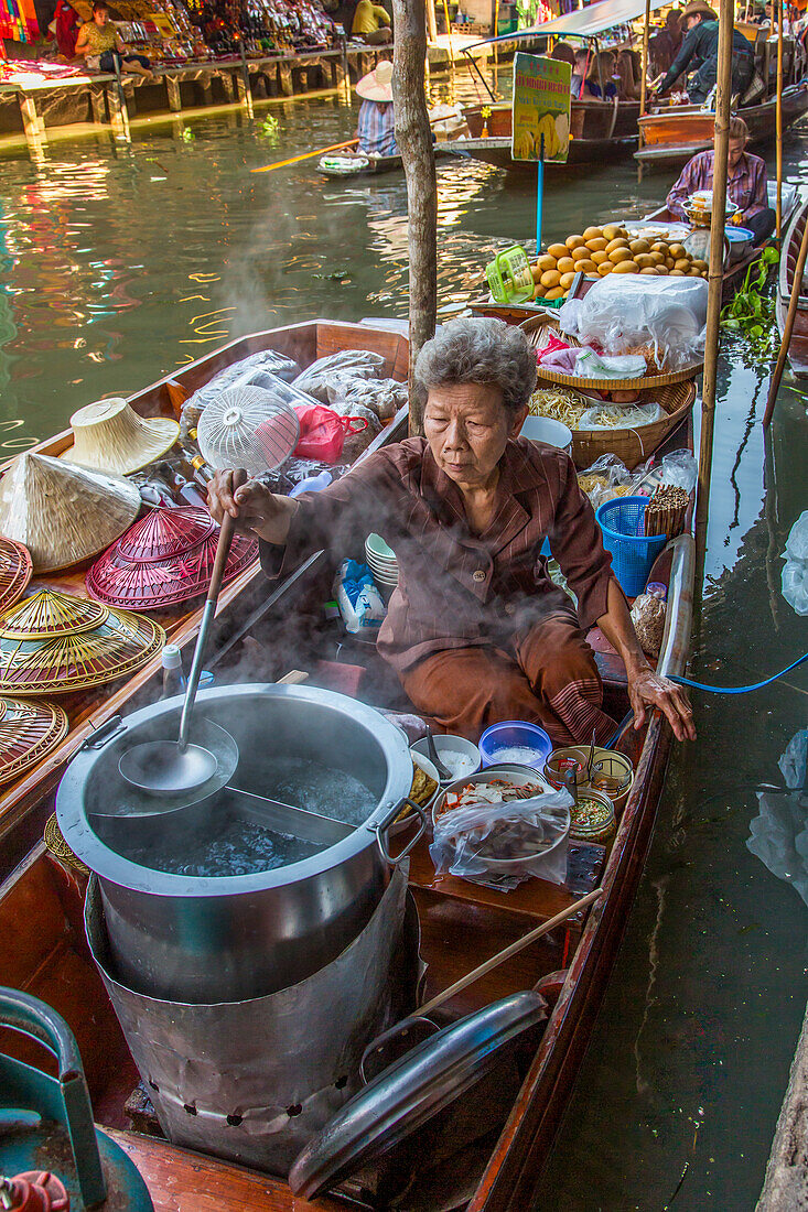 Eine thailändische Frau bei der Zubereitung von Speisen auf ihrem schwimmenden Küchenboot auf dem Damnoen Saduak Floating Market in Thailand