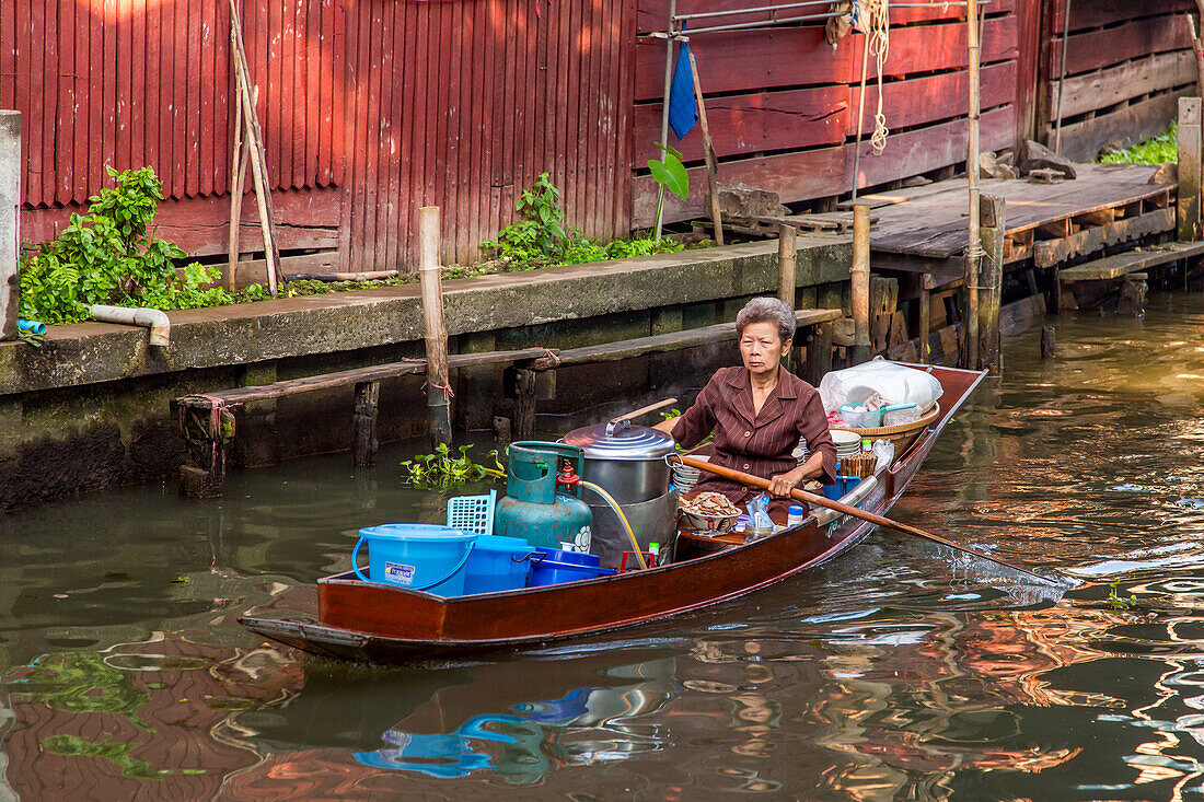 Eine thailändische Frau paddelt mit ihrem schwimmenden Küchenboot auf dem schwimmenden Markt von Damnoen Saduak in Thailand