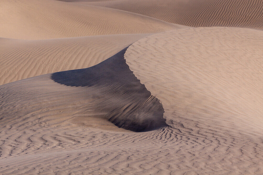 Sand weht vom Kamm einer Düne in den Mesquite Flat Sand Dunes in der Mojave-Wüste im Death Valley National Park, Kalifornien