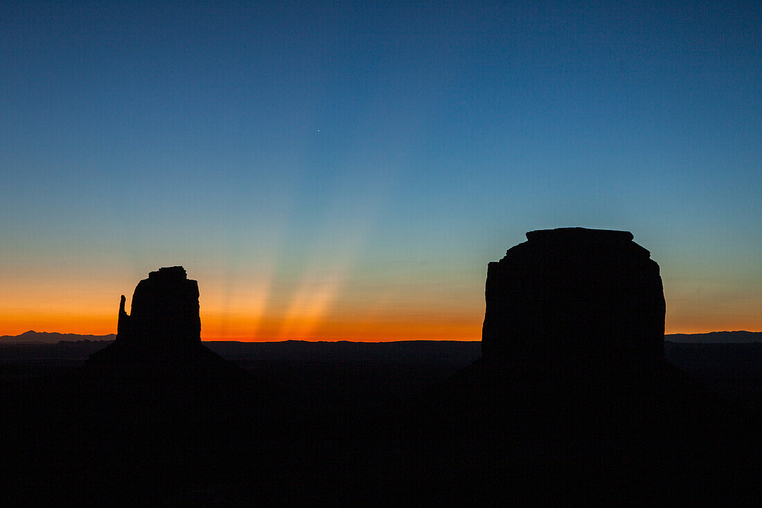 Crepuscular sun rays over the East Mitten & Merrick Butte before dawn in the Monument Valley Navajo Tribal Park in Arizona.