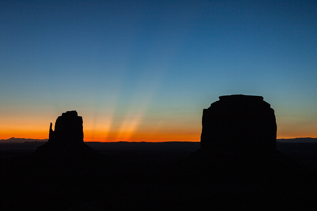 Dämmerungsstrahlen über dem East Mitten & Merrick Butte vor der Morgendämmerung im Monument Valley Navajo Tribal Park in Arizona