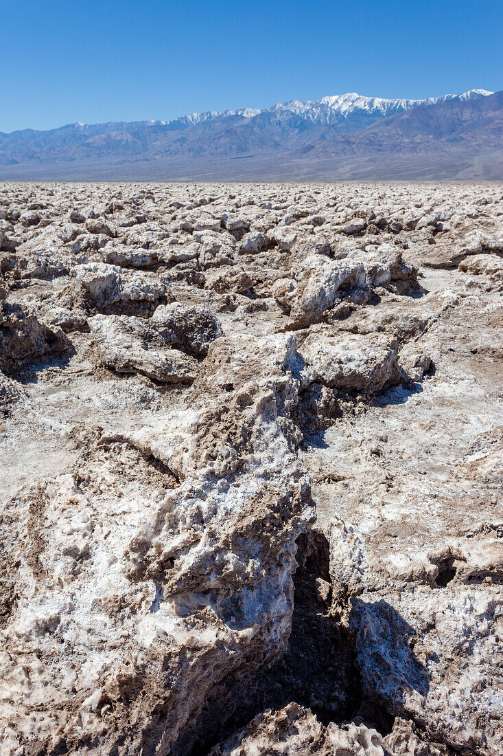 Jagged blocks of halite crystals in the Devil's Golf Course in the Mojave Desert in Death Valley National Park, California. The snow-capped Panamint Mountains in the distance.