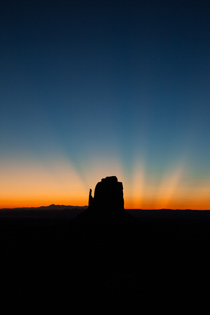 Crepuscular sun rays over the East Mitten before dawn in the Monument Valley Navajo Tribal Park in Arizona.