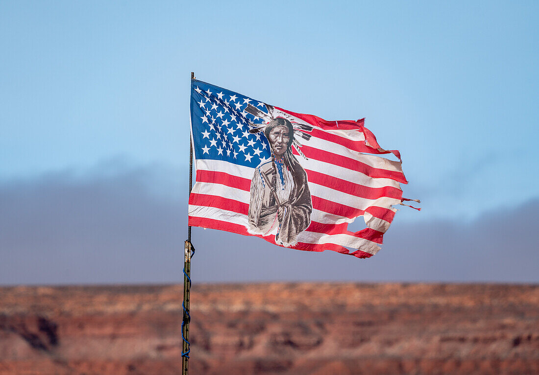 Eine zerfledderte amerikanische Flagge mit dem Bild eines Indianers in traditioneller Kleidung im Monument Valley Navajo Tribal Park in Arizona