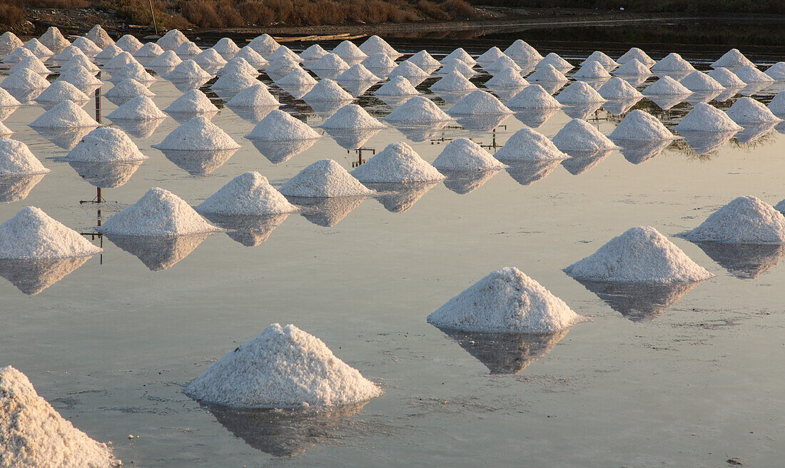 Piles of salt create geometric designs on the salt pan at a traditional evaporation salt farm in Samut Sakhon, Thailand.
