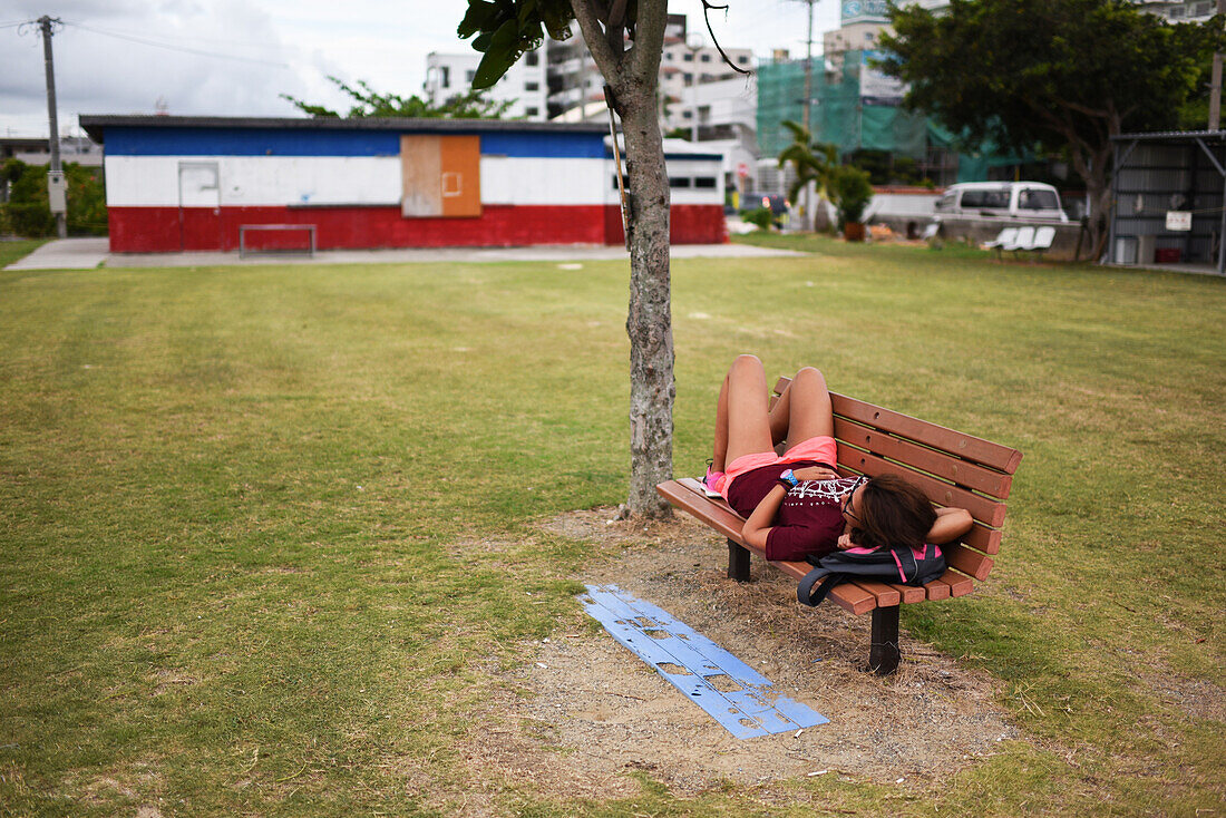 Junge Frau ruht sich auf einer hölzernen Parkbank aus, Ishigaki, Okinawa, Japan