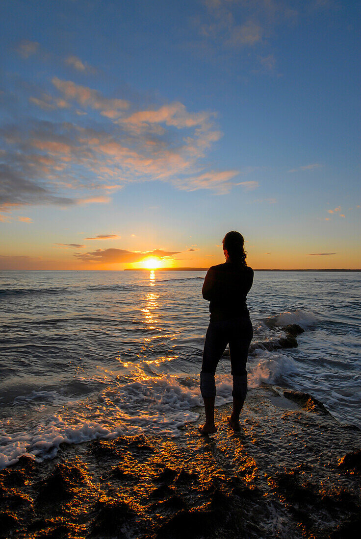 Silhouette einer jungen Frau, die einen wunderschönen Sonnenuntergang am Strand von Migjorn, Formentera, Spanien, genießt