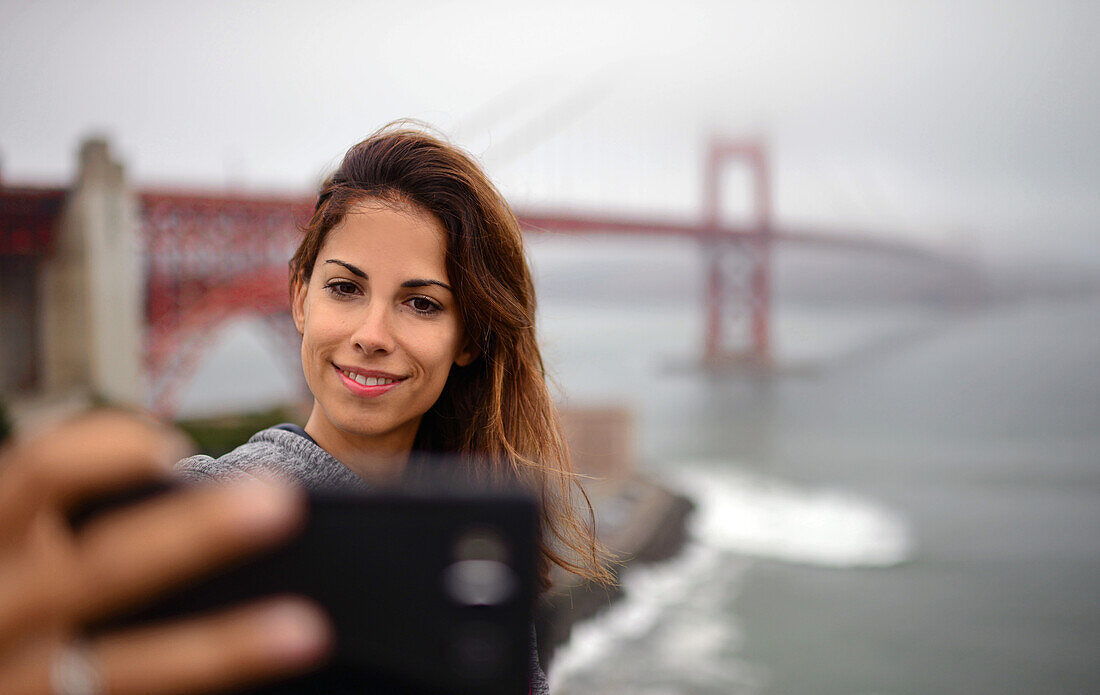 Junge Frau macht ein Selfie mit der Golden Gate Bridge, San Francisco