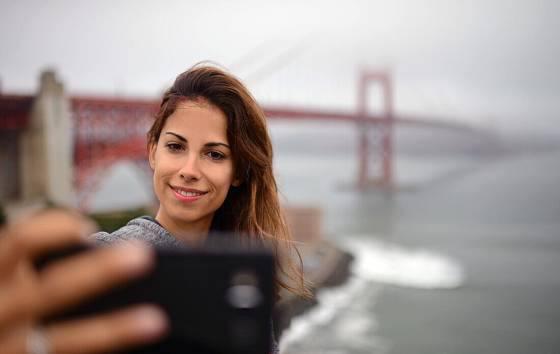 Young woman takes a selfie with Golden Gate Bridge, San Francisco.