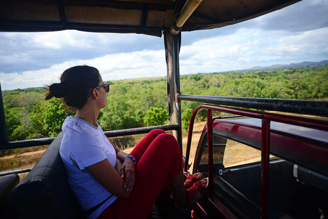 Junge Frau auf dem Dach eines Safari-Jeeps im Udawalawe-Nationalpark, an der Grenze zwischen den Provinzen Sabaragamuwa und Uva, Sri Lanka