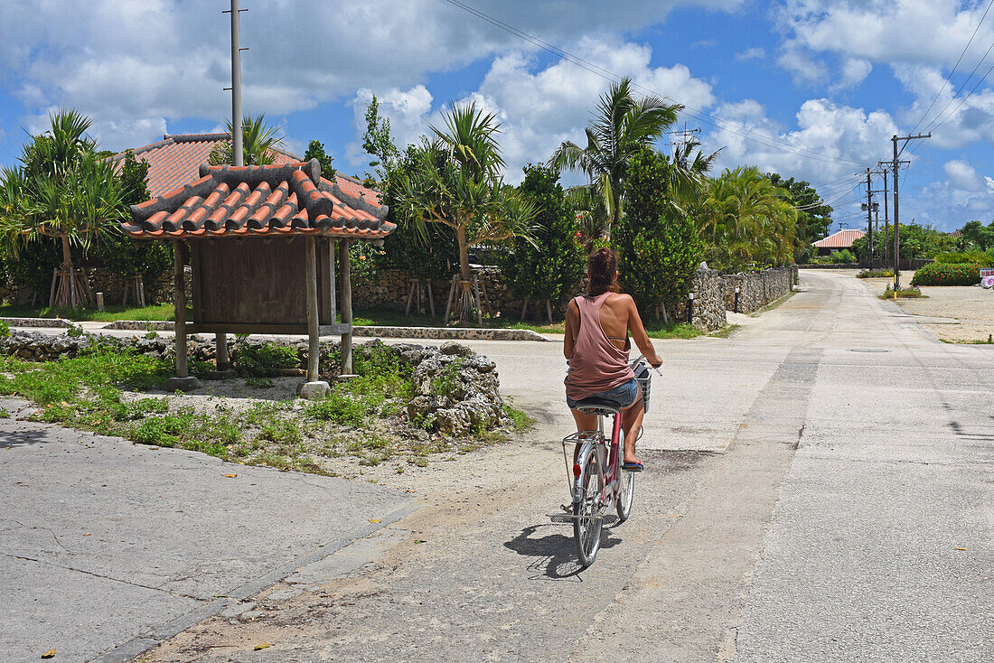 Junge Frau fährt Fahrrad auf der Insel Taketomi, Präfektur Okinawa, Japan