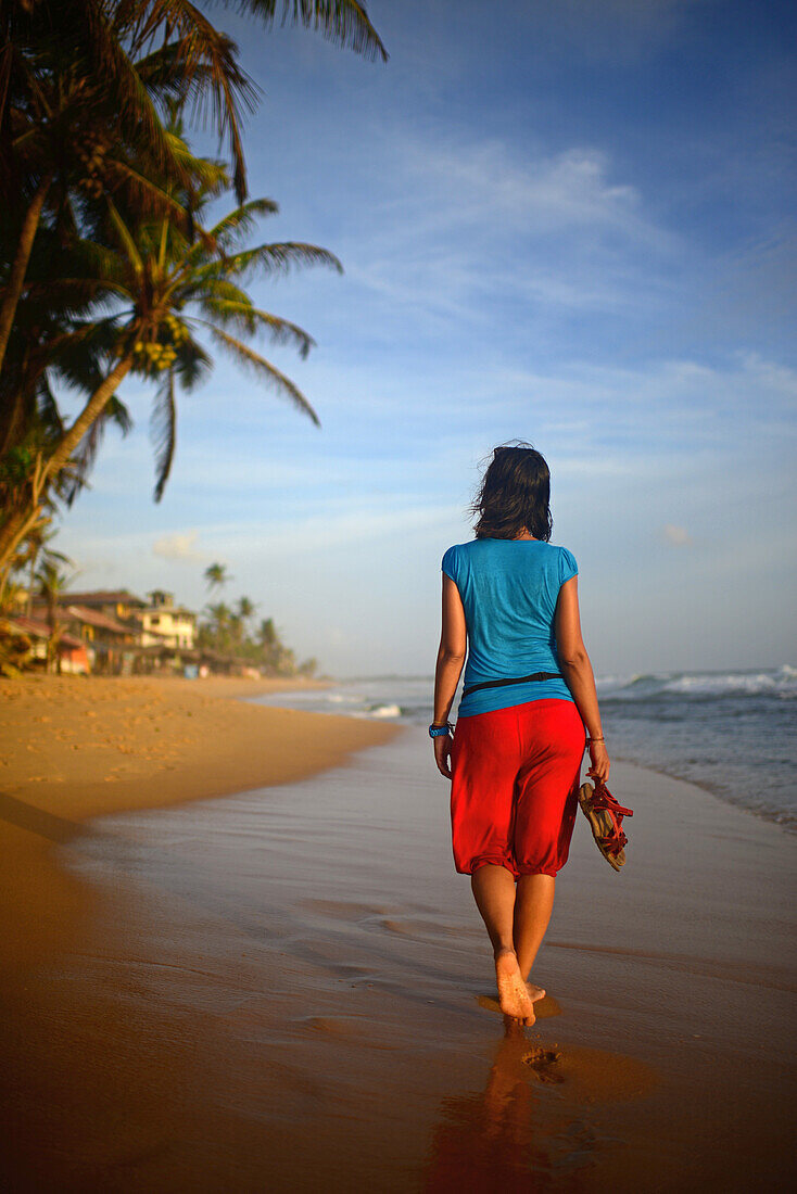 Young woman walking on Hikkaduwa beach at sunset, Sri Lanka