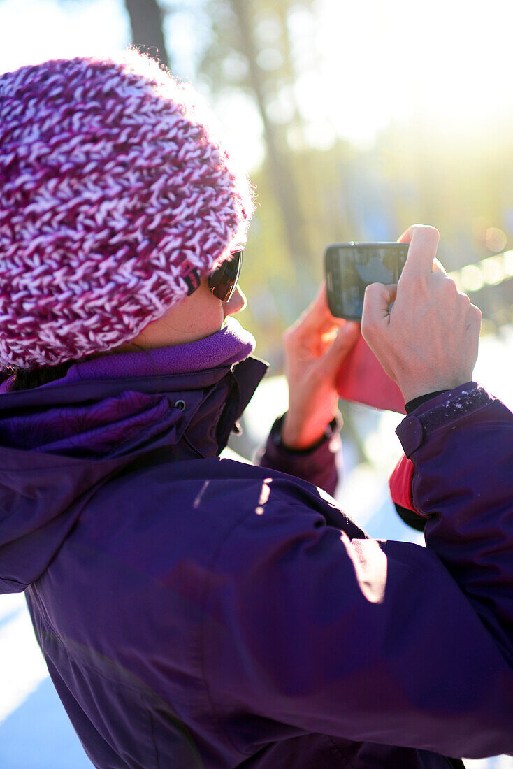 Junge attraktive Frau beim Fotografieren mit dem Mobiltelefon im Skigebiet Pyha, Lappland