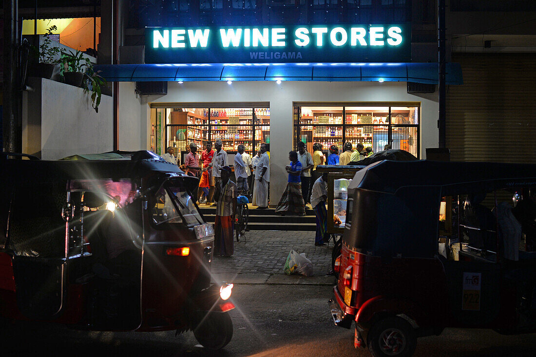 Menschen, die nachts in Weligama, Sri Lanka, in einem Laden für neuen Wein einkaufen