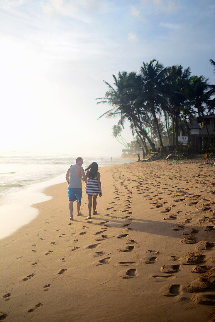 Paar spaziert bei Sonnenuntergang am Strand von Hikkaduwa, Sri Lanka