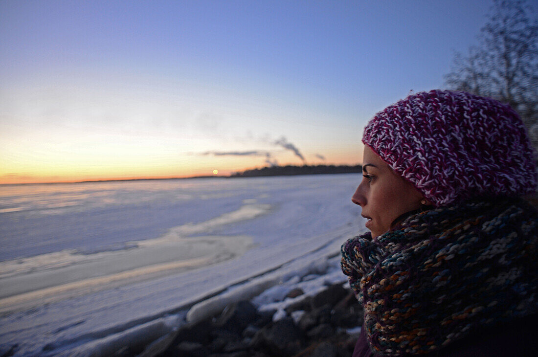 Entspannte junge Frau genießt den winterlichen Sonnenuntergang im Bottnischen Meerbusen, Kemi, Lappland