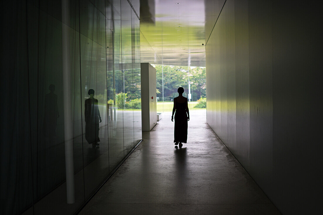 Silhouette of young woman walking in corridor, view from behind.