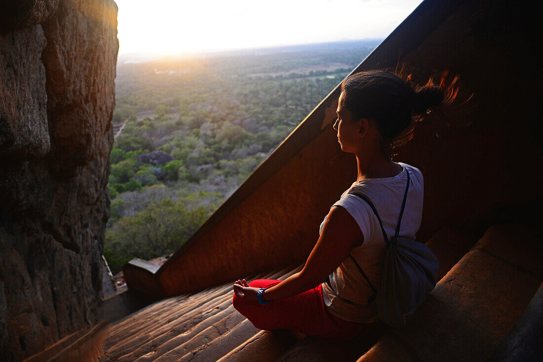 Junge Frau sitzt im Lotussitz auf der Treppe zur antiken Stadt Sigiriya, Sri Lanka