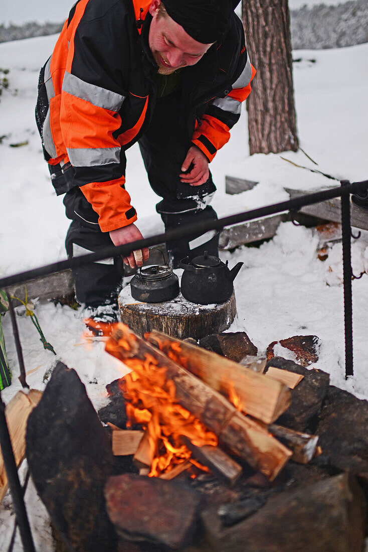 Antti, junger Reiseleiter von VisitInari, bereitet Kaffee und Tee auf einem Feuer in der Wildnis des Inari-Sees, Lappland, Finnland, zu