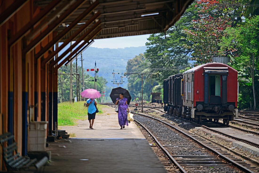 Two women with umbrellas walking in train station platform, Sri Lanka