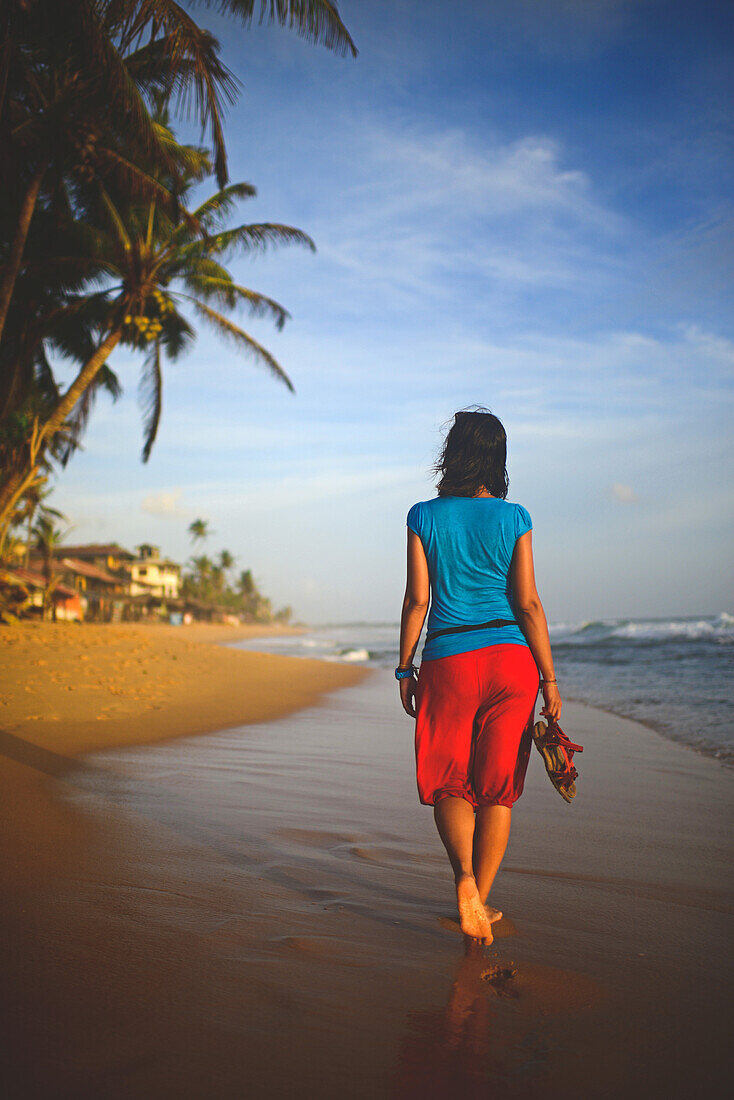 Young woman walking on Hikkaduwa beach at sunset, Sri Lanka