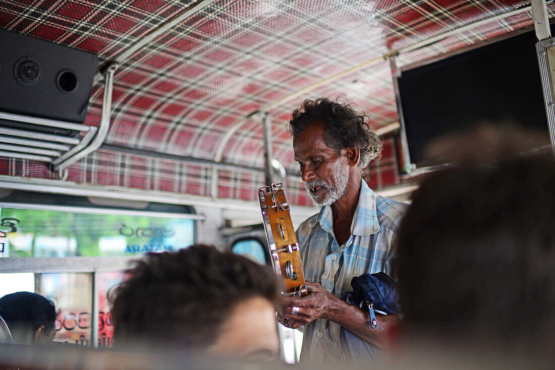 Ambulant musician playing tambourine inside a bus, Sri Lanka