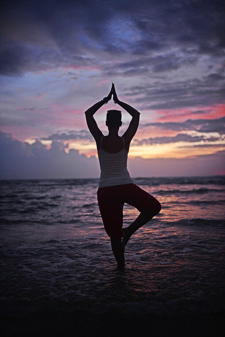 Young woman doing yoga tree pose at sunset, Hikkaduwa beach, Sri Lanka