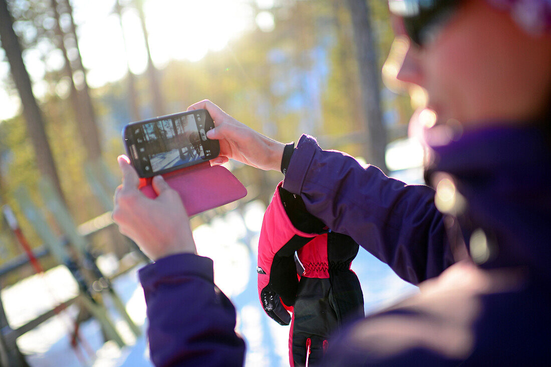 Junge attraktive Frau beim Fotografieren mit dem Mobiltelefon im Skigebiet Pyha, Lappland